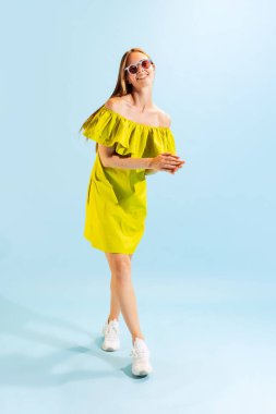 Happy girl. Studio shot of young beautiful blonde in summer yellow dress isolated on light blue background. Concept of beauty, art, fashion, youth, healthy lifestyle. Copyspace for ads, text, sales