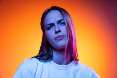 Dissatisfaction. Closeup face of young annoyed girl looking at camera isolated on orange color background in neon light. Concept of beauty, art, fashion, youth, sales and ad, education
