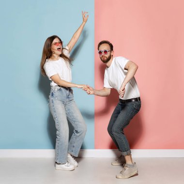 On style. Young stylish happy man and excited girl dancing hip-hop at studio on blue and pink trendy color background. Human emotions, youth, love and lifestyle concept