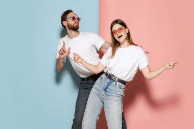 Party time. Young stylish happy man and excited girl dancing hip-hop at studio on blue and pink trendy color background. Human emotions, youth, love and lifestyle concept