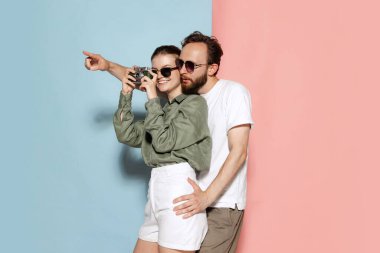 Taking picture. Happy couple in love, handsome man and charming girl posing isolated over blue-pink background. Fashion, emotions, youth, love, travel, vacation concept