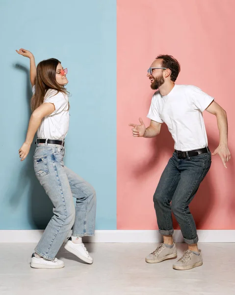 Dancing couple. Young stylish happy man and excited girl dancing hip-hop at studio on blue and pink trendy color background. Human emotions, youth, love and lifestyle concept