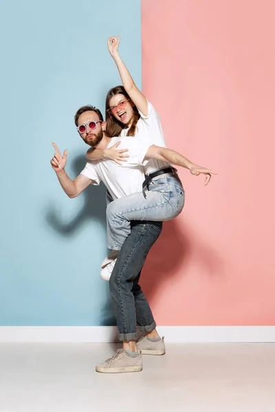 Euphoria. Portrait of crazy rock music fans, young couple wearing white t-shirts and jeans grimace and shout on pink-blue background. Concept of style, art, fashion and youth, ad