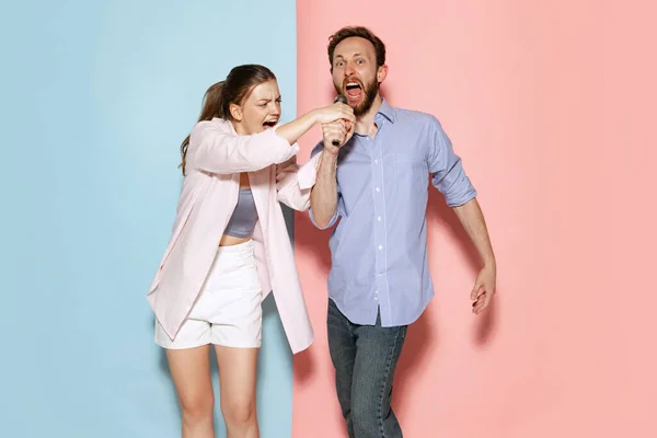 Singer. Couple of young funny and happy man and woman having fun isolated over blue and pink background. Human emotions, youth, love and active lifestyle concept