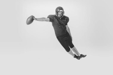 Falling down. Studio shot of american football player training with ball isolated on white background. Concept of sport, achievements, retro style. Monochrome