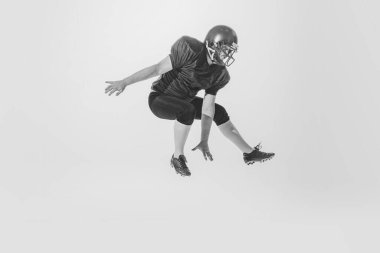 Training. Studio shot of american football player wearing sports uniform and helmet jumping isolated on white background. Concept of sport, achievements, retro style. Monochrome