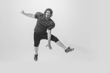 Training. Studio shot of american football player wearing sports uniform and helmet jumping isolated on white background. Concept of sport, achievements, retro style. Monochrome
