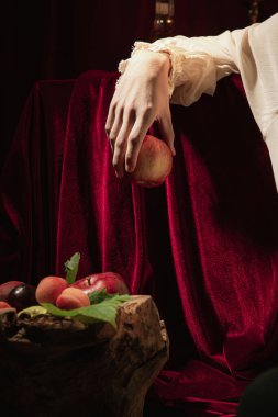 Closeup male hand with red apple over dark vintage background. Italian baroque style, art, creativity, vintage, comparison of eras concept.