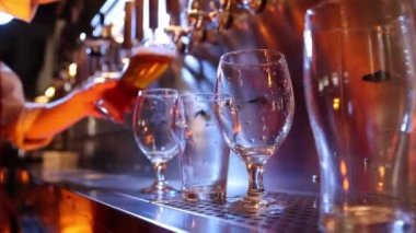 Bartender pouring beer into glasses at pub in neon light. Close-up view of barmans hand filling glass with light beer. Beer craft. Bar table. Oktoberfest, party, drinks, taste and alcohol concept.