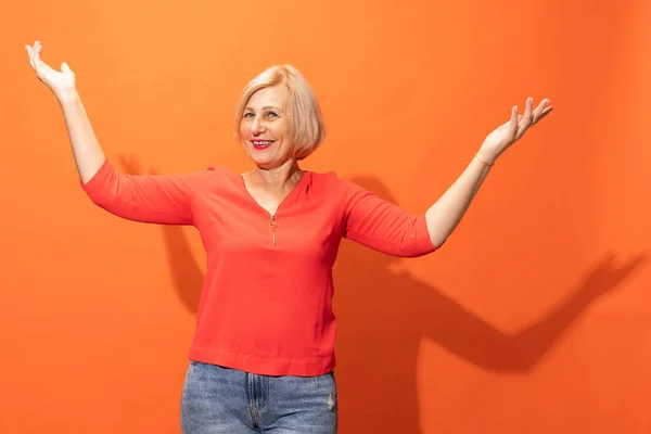 Wow, succes. One excited beautiful middle age woman with blond hair posing isolated on orange color background. Concept of natural beauty, ages, fashion, elder generation and ad