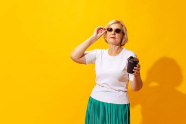 Fashion. Studio shot of fashionable senior woman in summer style outfit isolated on bright yellow background. Concept of beauty, emotions, vacation, travel, ad and sales