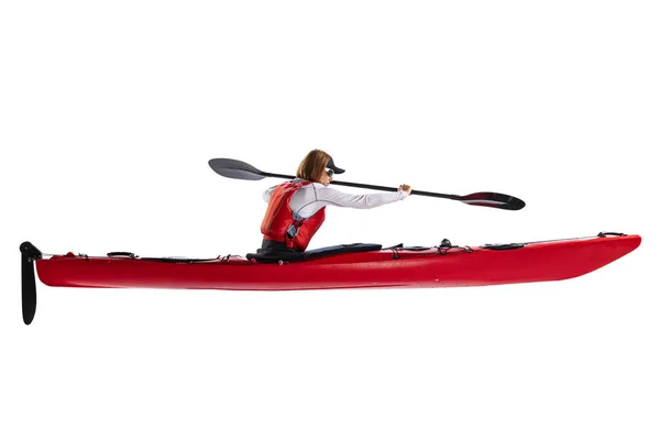 Profile view. Young woman, sportsman in red canoe, kayak with a life vest and a paddle isolated on white background. Concept of sport, nature, travel, active lifestyle