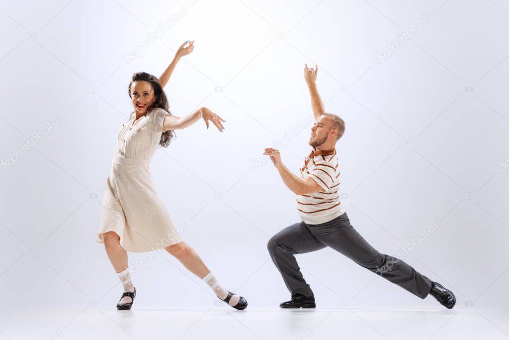 Music and dance. Astonished young man and woman in retro style outfits dancing lindy hop isolated on white background. Timeless traditions, 60s ,70s american fashion style. Emotions, expressions