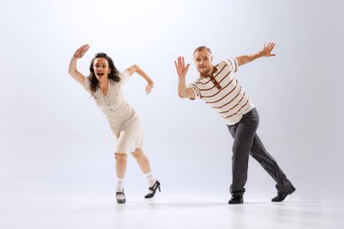 Müzik ve dans. Beyaz arka planda dans eden, dans eden, Lindy Hop kıyafetli genç adam ve kadın hayrete düştü. Zamansız gelenekler, 60 'lar, 70' ler Amerikan moda tarzı. Duygular, ifadeler.