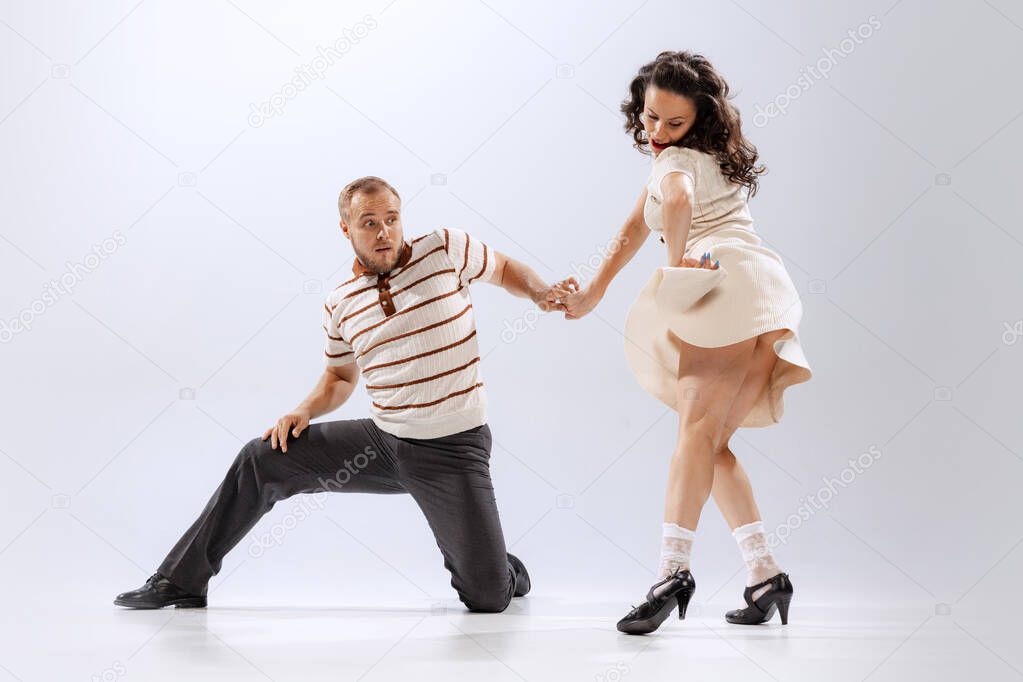 Rhythm and expression. Energetic dance couple in retro style outfits dancing lindy hop, jive isolated on white background. Timeless traditions, 60s ,70s american fashion style. Emotions, expressions