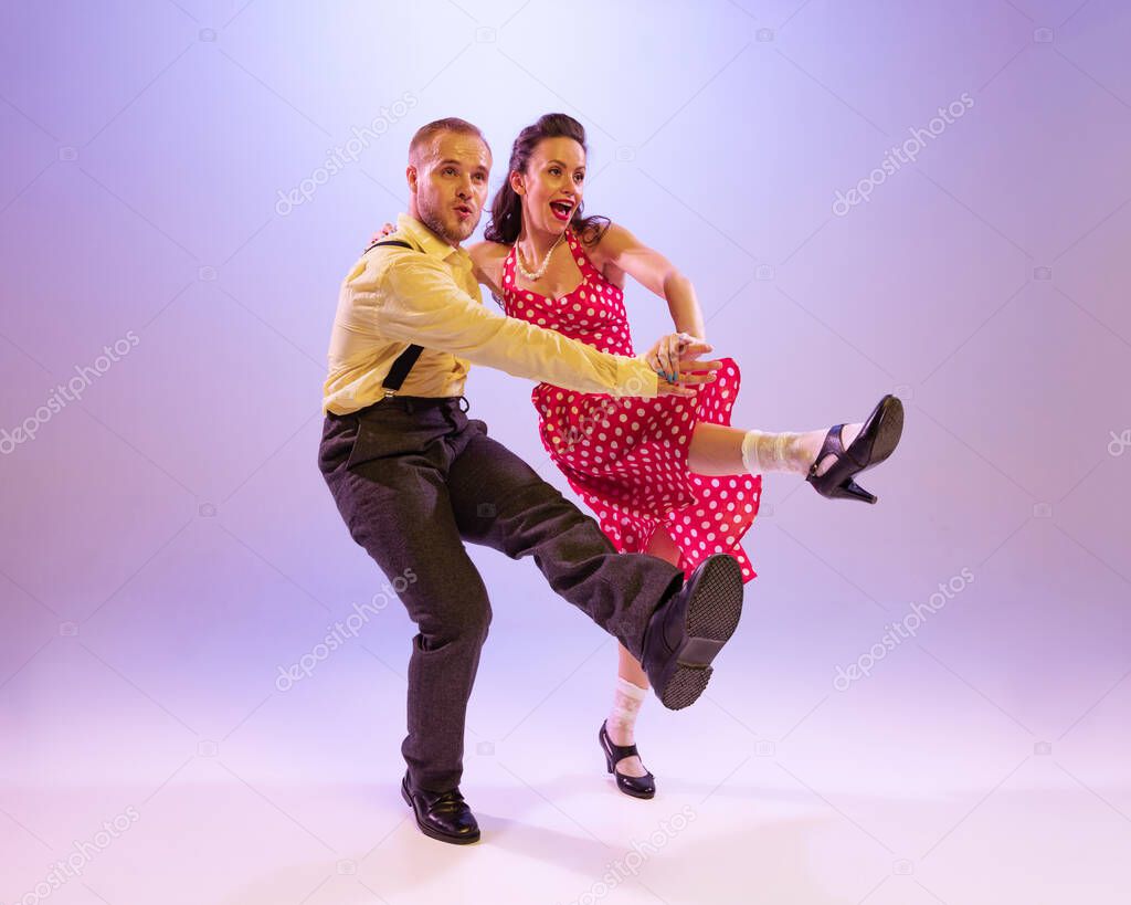 Emotional bright couple of dancers in colorful retro style attires dancing incendiary dances isolated on purple background in neon light. Concept of art, 60s, 70s american culture