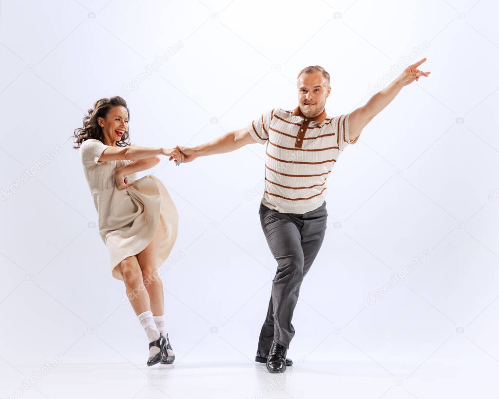 Emotions, expressions and feelings in movements. Dynamic portrait of emotional man and woman dancing sport dances isolated on white background. Timeless traditions, 60s ,70s american fashion style.