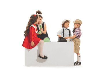 Group of cheerful kids, little boys and girls in retro style summer outfit playing with vintage phones isolated on white background. Concept of emotions, facial expression, fun, childhood. Copy space