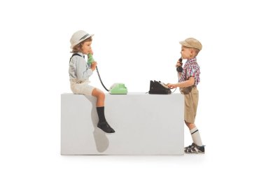 Ring to parents. Portrait of two cheerful kids in retro style summer outfit using vintage phone isolated on white background. Concept of emotions, facial expression, fun, childhood. Copy space for ad