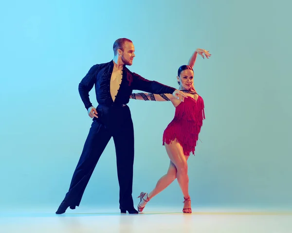 Paso doble. Studio shot of young couple, professional dancers dancing ballroom dance isolated on blue background. Concept of art, dance, beauty, music, style. Copy space for ad. International Dance