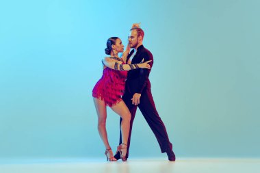 Paso doble. Studio shot of young couple, professional dancers dancing ballroom dance isolated on blue background. Concept of art, dance, beauty, music, style. Copy space for ad. International Dance