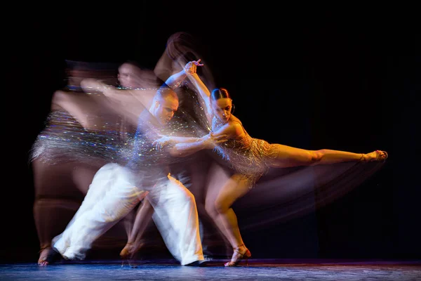 Energy in movements. Two professional dancers dancing ballroom dance isolated on dark background with mixed light. Concept of art, dance, beauty, music, style. International Dance Day