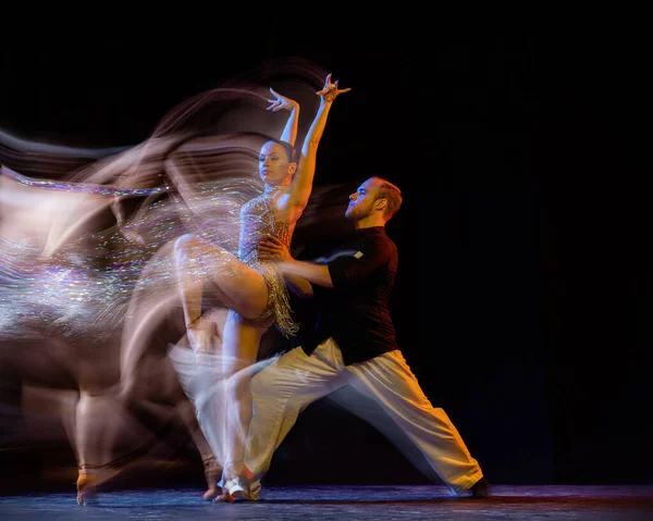 Flight of feelings. Two professional dancers dancing ballroom dance isolated on dark background with mixed light. Concept of art, dance, beauty, music, style. International Dance Day