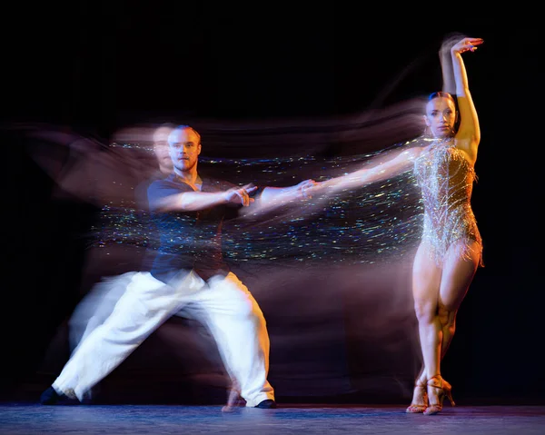 Energy in movements. Two professional dancers dancing ballroom dance isolated on dark background with mixed light. Concept of art, dance, beauty, music, style. International Dance Day