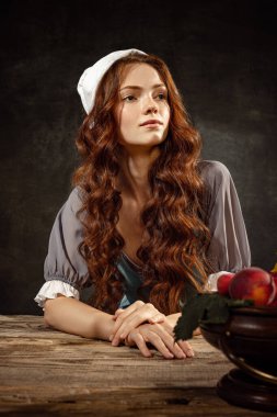 Vintage portrait of young adorable redhead girl in image of medieval person, peasant woman in renaissance style dress isolated on dark background. Comparison of eras, beauty, history, art, creativity.