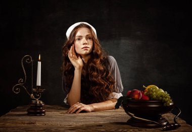 Hope. Creative portrait of young beautiful redhead girl in image of medieval person in renaissance style dress isolated on dark background. Comparison of eras, beauty, history, art, creativity.