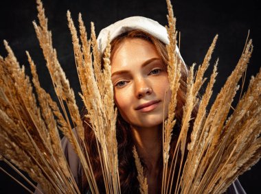 Tenderness. Closeup young charming redhead girl in image of medieval person in renaissance style in ears of wheat. Comparison of eras, beauty, history, art, creativity.