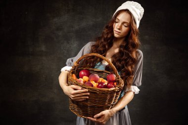 Harvest. Portrait of charming redhair girl with long curly hair like girl of renaissance eras, lady-peasant isolated on dark background. Comparison of eras, beauty, history, art, creativity.