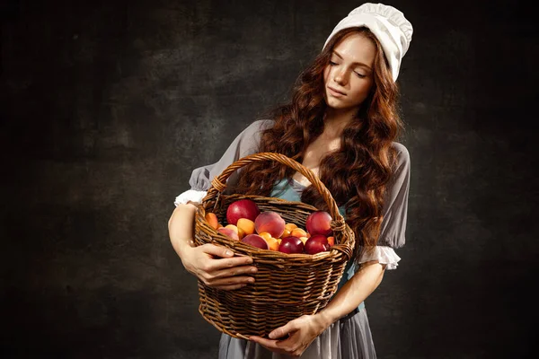 Harvest. Portrait of charming redhair girl with long curly hair like girl of renaissance eras, lady-peasant isolated on dark background. Comparison of eras, beauty, history, art, creativity.