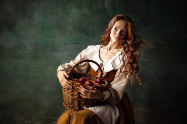 Girl with plums. Young charming redhair girl with long curly hair like girl of renaissance eras isolated on dark background. Comparison of eras, beauty, history, art, creativity.