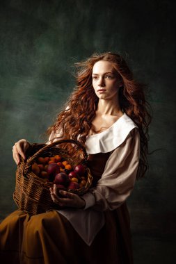 Young beautiful redhair girl with long curly hair like girl of renaissance eras isolated on dark background. Comparison of eras, beauty, history, art, creativity.