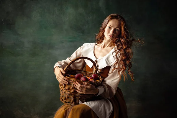 Girl with plums. Young charming redhair girl with long curly hair like girl of renaissance eras isolated on dark background. Comparison of eras, beauty, history, art, creativity.