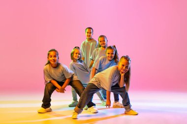 Joy, fun and happiness. Portrait of cheerful, active little girls, happy kids dancing isolated on orange background in neon light. Concept of music, fashion, art, childhood, hobby.