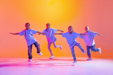Joy, fun and happiness. Portrait of cheerful, active little girls, happy kids dancing isolated on orange background in neon light. Concept of music, fashion, art, childhood, hobby.
