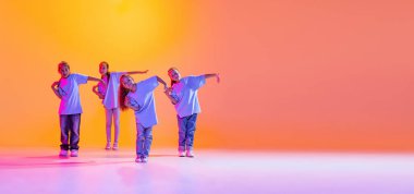 Modern choreography lesson. Dance group of happy, active little girls in t-shirts and jeans in action isolated on orange background in neon. Concept of music, fashion, art, childhood, hobby. Flyer