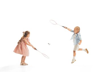 Portrait of two little children, boy and girl playing together in badminton, posing isolated over white studio background. Concept of childhood, game, school, fun, education. Copy space for ad