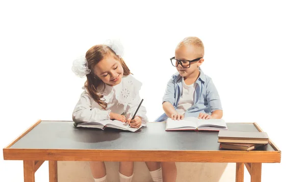 Portrait of little boy and girl, children sitting at desk and studying, doing homework isolated over white background. Concept of childhood, game, school, fun, education. Copy space for ad