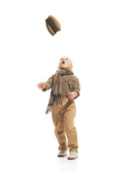 Portrait of little boy, child in retro suit throwing cap upwards, posing isolated over white studio background. Autumn fashion. Concept of childhood, game, school, fun, education. Copy space for ad