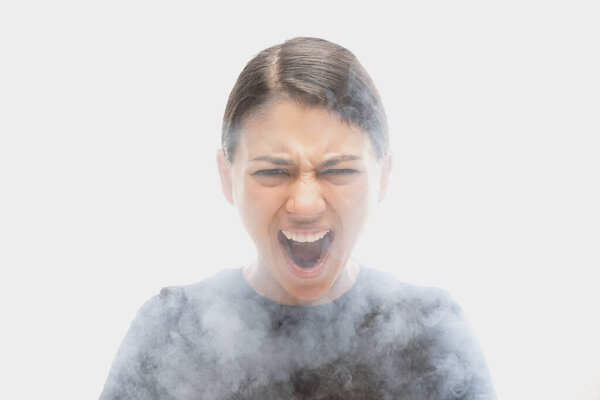 Shouting young dark hair woman with different emotions isolated over white background with clouds of smoke. Concept of mental health, art, human emotions, challenges, ad