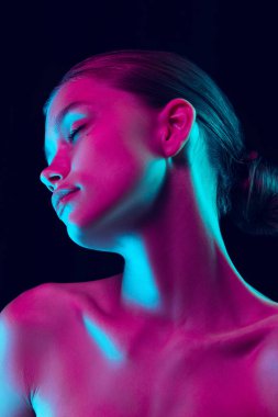 Perfection. Portrait of tender young woman with well-kept skin posing isolated over dark background in neon light. Concept of natural beauty, art, emotions, cosmetics and youth