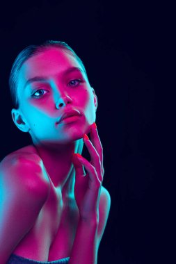 Fashion, style. Young beautiful girl with well-kept skin and without makeup isolated over dark background in neon light. Concept of natural beauty, art, emotions, cosmetics and youth
