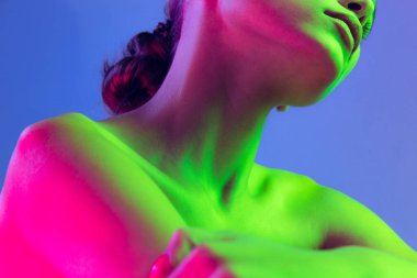 Close up female neck, collarbones and shoulders in pink neon light over dark background. Beautiful young womans body with well-kept skin. Beauty, fitness, diet, spa, aesthetic cosmetology