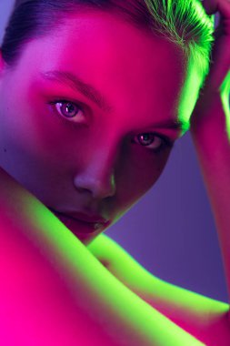 Femininity and confidence. Portrait of young, beautiful and healthy girl with well-kept skin isolated on dark background in neon light. Art, fashion, style, facial expression, eco products and health