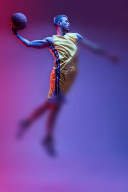 Slam dunk. Portrait with blurring effect of athletic male basketball player training isolated in neon light on purple background. Concept of health, professional sport, hobby.