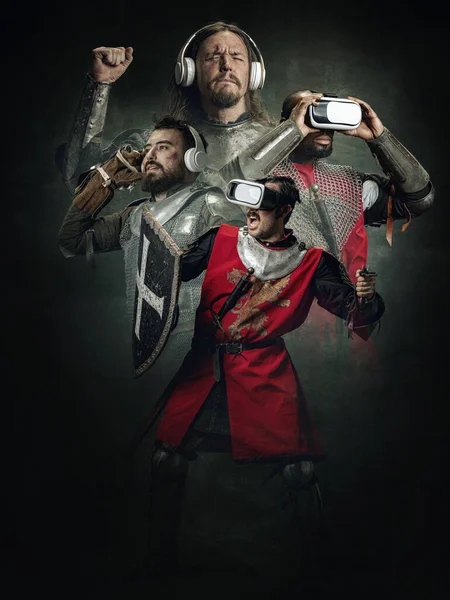 Technologies of the future in the past. Creative poster with brutal serious medieval warriors in war clothes and VR headsets over dark vintage background. Comparison of eras,