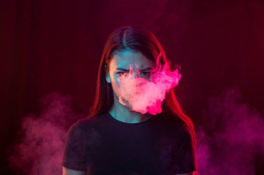 Angry young girl with dark hair releases smoke from the mouth isolated over pink background. Concept of mental health, art, human emotions, challenges, ad